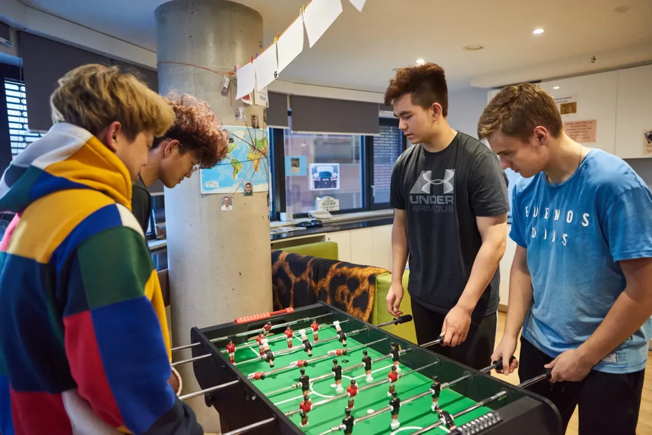 Four boys playing foosball in common room