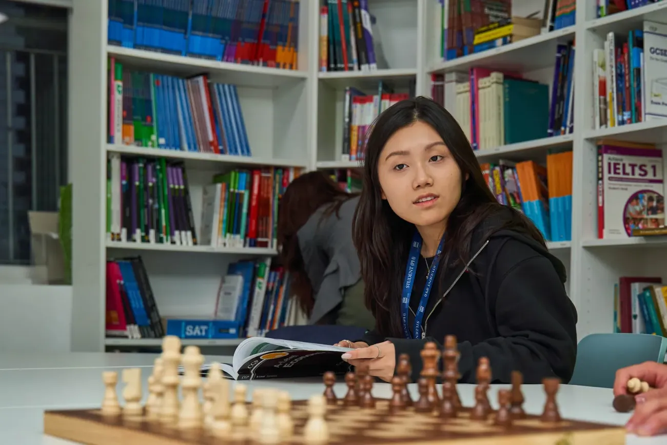 Student reading book beside chess board
